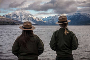 Two national park rangers looking at water with mountains in the distance